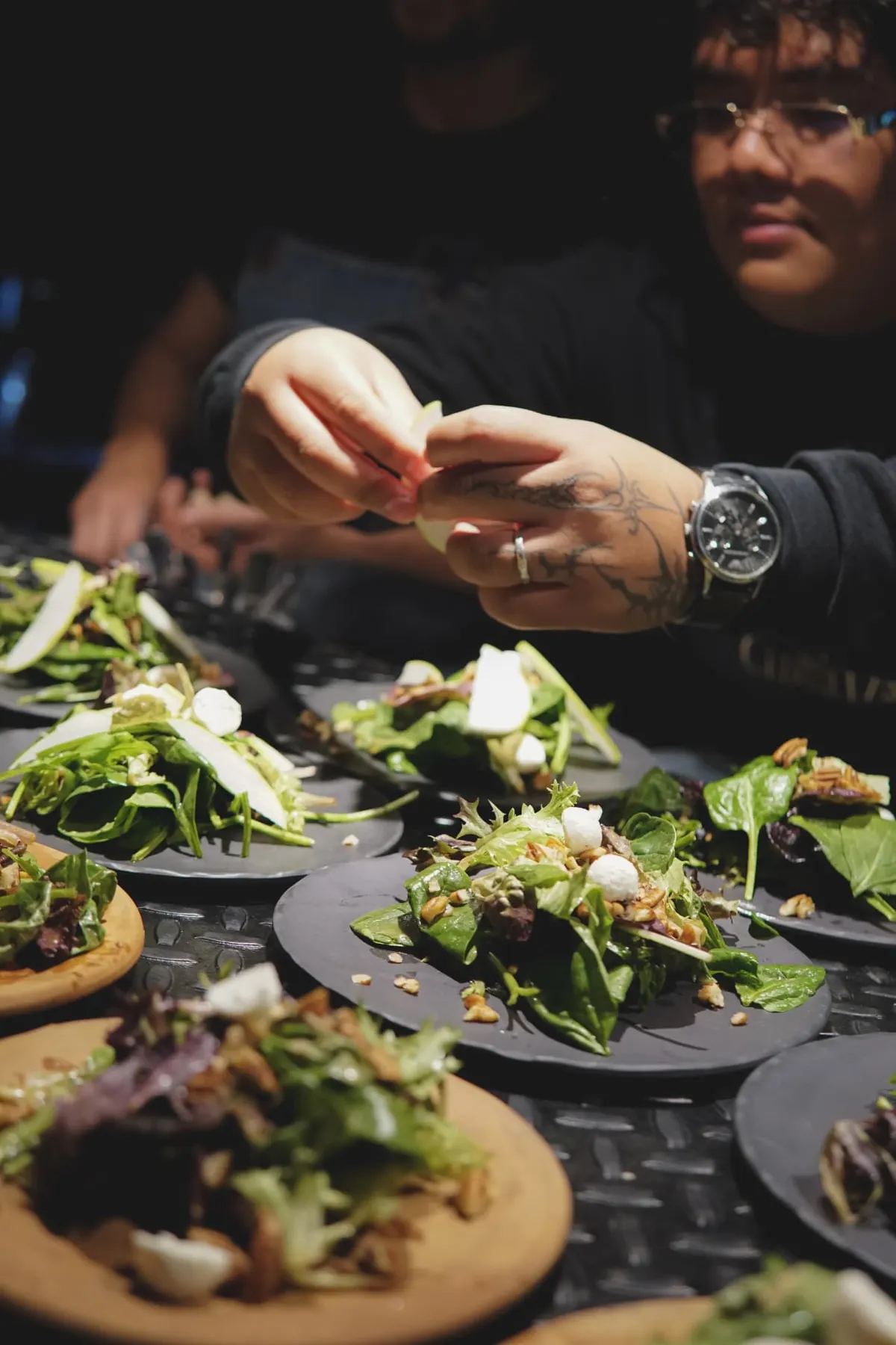 Chef plating seasonal greens on black clay plates